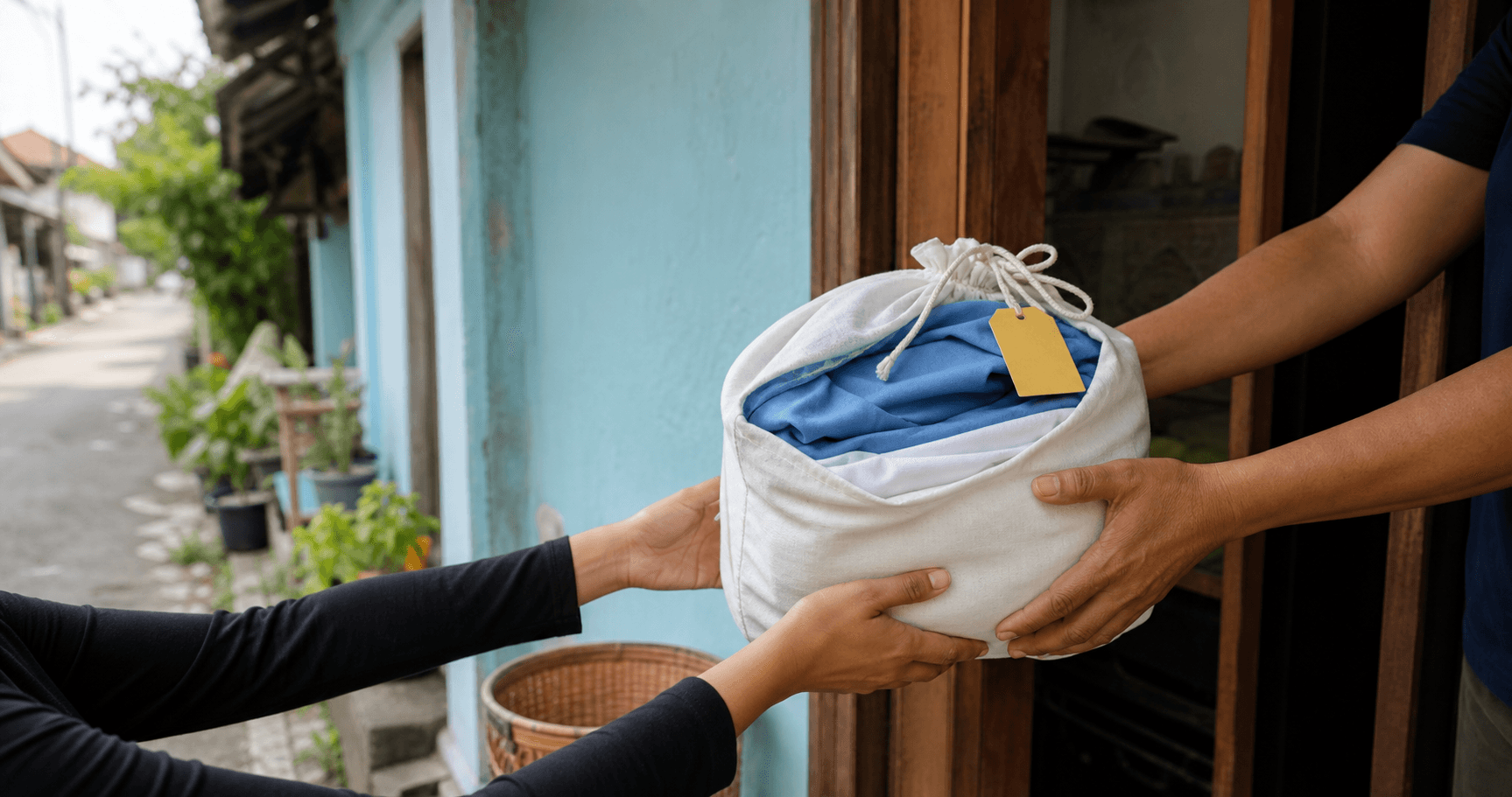 Serah terima kantong laundry berisi pakaian biru dan putih di depan rumah